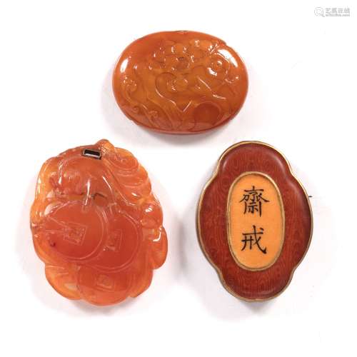 Three amber pendants Chinese, 19th Century variously carved and one of quatrefoil form with