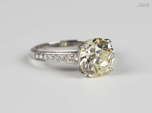 A platinum and diamond ring, claw set with the principal light yellow tinted round brilliant cut