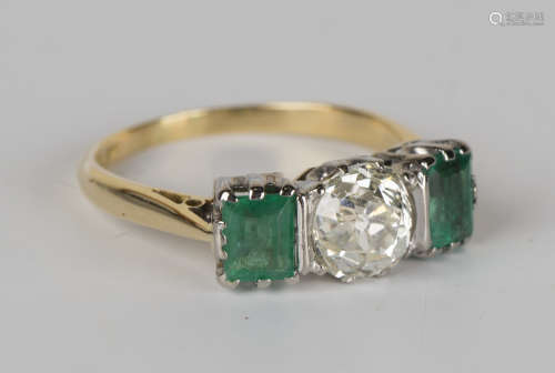 A platinum, 18ct gold, emerald and diamond three stone ring, claw set with a circular cut diamond