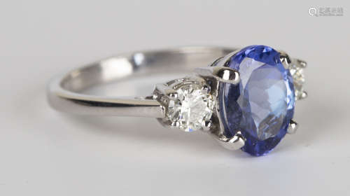 A white gold, sapphire and diamond three stone ring, claw set with an oval cut sapphire between