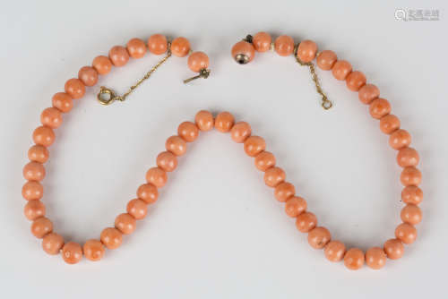 A single row necklace of fifty-six coral beads on a coral bead clasp, fitted with a safety chain,