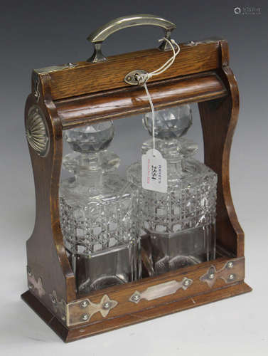 An Edwardian oak and plate mounted two bottle tantalus, fitted with a pair of square cut glass