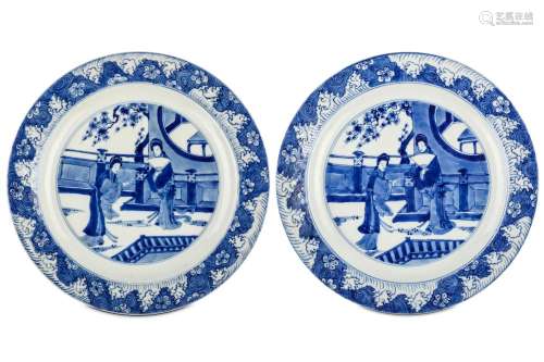 A PAIR OF CHINESE BLUE AND WHITE ‘LADIES’ DISHES. Kangxi. Each with a central roundel enclosing two ladies on a garden veranda below flowering prunus branches, within a border of prunus flower heads borne on swirling and frothing waves, six