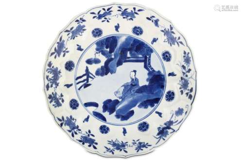 A CHINESE BLUE AND WHITE 'SCHOLAR' DISH. Kangxi mark and of the period. The central roundel painted with a scholar beneath pines and rocks, within a border of lobed lappets enclosing flower heads and a further band of floral spray beneath the foliate