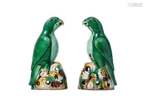 A PAIR OF CHINESE GREEN GLAZED PARROTS. Kangxi. The parrots in mirror image, covered in a green glaze and perched on a pierced rocky base, covered in an egg and spinach glaze, 19cm H. (2) 清康熙   綠釉鸚鵡一對