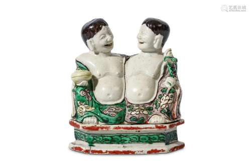 A CHINESE BISCUIT FIGURE OF THE TWINS ‘HEHE ERXIAN’. Kangxi. Well modelled seated side by side, with bare chests, the robes covered in yellow, green and aubergine enamels, 12cm H. 清康熙   素燒三彩合和二仙像