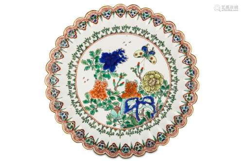 A CHINESE FAMILLE VERTE ‘FLOWER AND BUTTERFLY’ MOULDED DISH. Kangxi. Brightly enamelled in green, blue, orange and yellow, the central roundel enclosing peonies emerging from behind ornamental rockwork among butterflies and insects within an