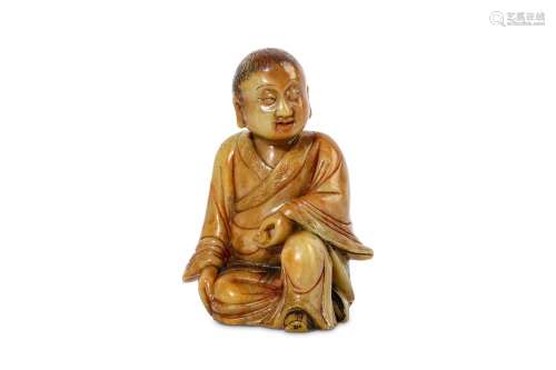 A CHINESE SOAPSTONE CARVING OF A BOY. Kangxi. Seated in long flowing robes, the left hand holding a small ball and supported on the raised left knee, the right leg tucked beneath, the head turned slightly to the left, the robes incised with lingzhi