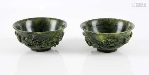 Pair of Chinese spinach green jade bowls decorated with dragons, on round feet, each 10cm diameter,