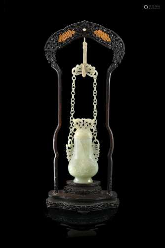 A celadon jade vase and cover hanged with chain to an ivory dragon-shaped hook in a decorated wood
