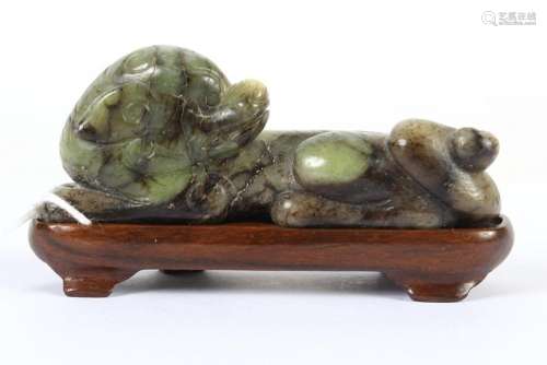CHINESE HARDSTONE CARVING OF A FU DOG - Recumbent Fu Dog carved in mottled green hardstone; on a fitted stand Unsigned. Good condition.