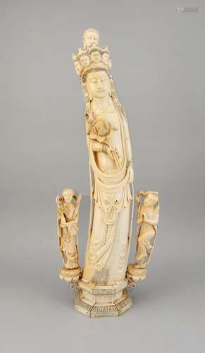 Große Elfenbeinfigur, China, um 1900, Guanyin?, Frau mit einem Kranz aus Frauenköpfen bekrönt, aus welchem wiederum ein Buddha-Kopf hervorgeht. In der rechten Hand eine Lotosblüte haltend. Auf oktogonalem, zweistufigen Sockel/Postament mit Flammen- und Wolkenband-Reliefs. Zu beiden Seiten wächst eine Lotosblüte aus dem Sockel, der zwei weiteren, kleineren Figuren (Stifterfiguren?) als Stand dient. Figur und Sockel mit geschwärzten Ritzdekoren. Alle 3 Figuren von ihren Sockeln gelöst, H. 74 cm