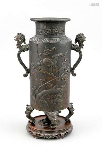 A 19th-century Chinese bronze vase, of cylinder form on 4 rolled-up tongue legs, recto and verso with flower and bird relief decor, handles with phoenix heads, short neck with cloud band decor, flared border, on 5-feet wood base with wire inlays, h. 28 cm (without base)