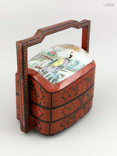 A 19th-century Chinese lunch pail, wood with red lacquer incised with ornaments, porcelain cover polychromed onglaze (famille rose), carrying handle, ca. 34 x 31 x 22 cm