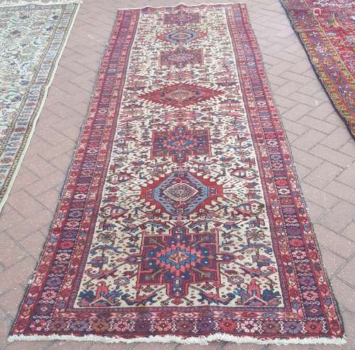 A Persian Heriz runner, geometric medallions and stylised motifs on cream ground with boteh