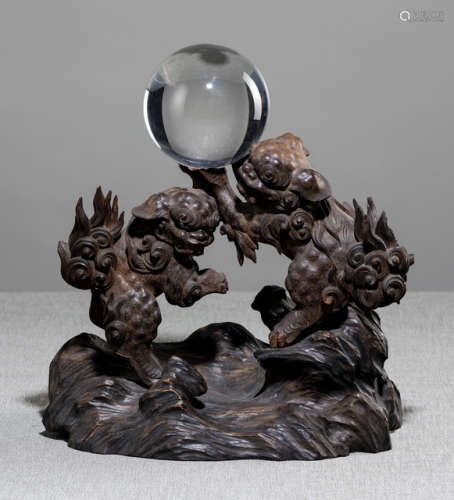 A CARVED WOOD OKIMONO WITH A CRYSTAL BALL RESTING ON TWO SHISHI MOUNTED TO A CARVED WOOD STAND IN SHAPE OF A ROCK