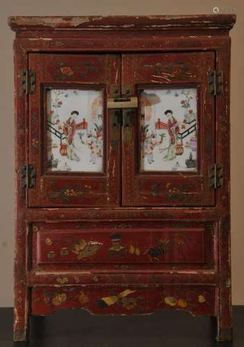 Small cabinet. China. Early 20th century. Surface with red and gold lacquer decoration. Front with two Famille Rose panels of women and children.   27