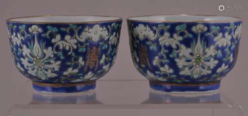 Pair of porcelain cups. China. Early 20th century. Blue ground decorated with stylized flowers, bats and shou characters. Tongzhi mark and period. Mark in red on the base. 1-3/4