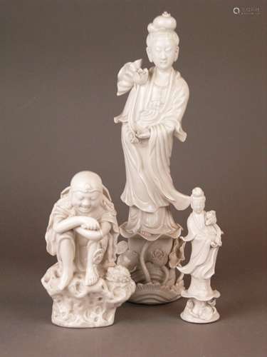 3 Blanc-de-Chine figures - China 20th century, glazed white porcelain, 1x Guanyin, finely<br />elaborated  figure of the goddess of charity, lotus blossom in the right hand, standing on a base washed round with waves, backside is marked, H. ca.34,5cm; 1x small Guanyin  on a high pedestal with fullplastic lotus ornament, H.ca.16cm; 1x  Liu Hai, figure of the cheerful immortal shown crouching on a rockwork base, holding a long string of cash, a large broad brimmed straw hat dangles at his back, with the three legged toad to his right side, H.ca.18.5cm