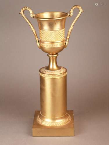 Pokal - Messing vergoldet, über quadratischem Sockel (Holzkern ummantelt) Säulenschaft,<br />darauf ein Kelchkrater mit hochgezogenen Drachenkopfhenkeln, ziergravierte Ornamentbänder, H.ca.44,5cm, Standunterseite mit Samtbezug