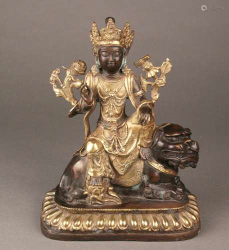 Manjushri seated on a Lion - China, gilt bronzed brass casting, some copper efflorescence,<br />the Bodhisattva of Wisdom shown seated in lalitasana on a Buddhist lion and wearing long robes, lotus pedestal with lotus leaf frieze, lushly adorned with jewels and a large crown on the head, next to his left shoulder blossoms a lotus carrying a sutra book, saddlecloth engraved, closed bottom, H.c.24,5cm