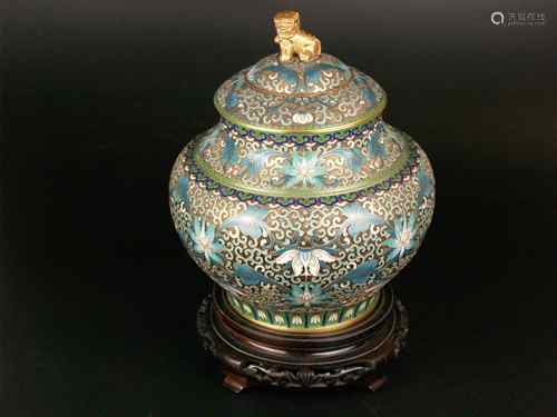 Cloisonné lid vase - bulbous body, brass with polychrome cloisonné relief decoration with<br />flowers, blue glazed inside, gilt fo-dog as lid knob, on a carved wooden base with four feet, H. (without base): approx.22cm