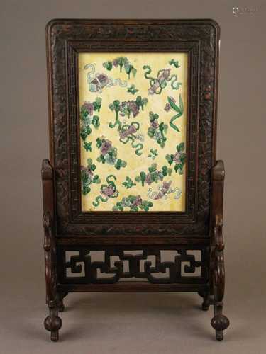 Table screen with ceramic plate - China, rectangular ceramic plate with enamel painting,<br />treasures and lotus flowers on yellow background, ca.37,5x15,5cm, in carved frame, openwork frame with curly ornamental elements, 1 base restored, glued, H / L.ca.26,5cm