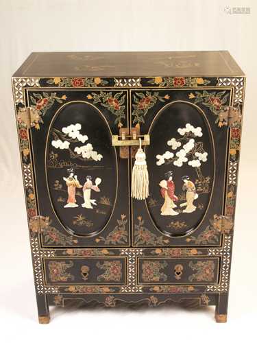 Black lacquer cabinet - China, 2nd half of the 20th century, rectangular body on square<br />legs, two-door, below that two drawers, a fixed shelf inside, with floral (gold lacquer) painting and framing of diamond-shaped pearl inlays, oval  curly door and side fillings with different colored stone inlays, the front depict ladies under the trees, each side with bird on fruit tree branch (peach or pomegranate tree, faces partly made of bone, partially plastic additions, chased brass fittings and lock with tassel, about 101.5x 76x38 cm , on the reverse manufacturer label / China, slight traces of usage