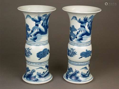 A Pair of Underglaze Blue Chinese Gu Vases - porcelain, Qing Dynasty (1644-1912), painted<br />with shan shui landscapes, floral motifs and ''han wen'' borders in underglaze blue, 6-character kaishu mark ''Da Qing Kangxi Nian Zhi'' in a double ring to the base, appr.11,41 in./ 29cm high