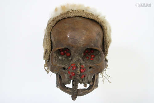 old original Papua New Guinean Asmat sculpture with a ‘Ndambirkus’ skull with red seeds (eyes and nose) and a head’s ornament made of vegetal fibres and the skin of a koeskoes