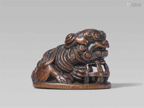 A large wood seal-type netsuke of a shishi. 19th centurySeated on a flat oval base, its chin resting