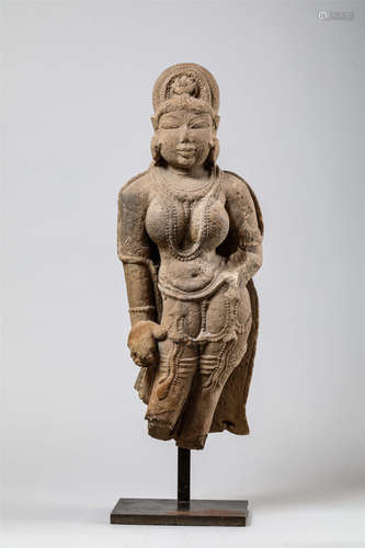 Lakshmi figurée   nue debout en léger tribanga, parée de joyaux perlés et de larges pendants   d'oreilles, coiffée d'un haut chignon maintenu par un   diadème en arc de cercle incorporant la tête du lion Narasimha, l'un des avatars de Vishnu son époux, couverte d'un voile retombant sur ses épaules jusqu'à mi-cuisses. Pierre grès beige. Inde. Période post Gupta. 7 ème à 8 ème siècle. 57cm.Accidents, cassures et manques. Ancienne collection française.