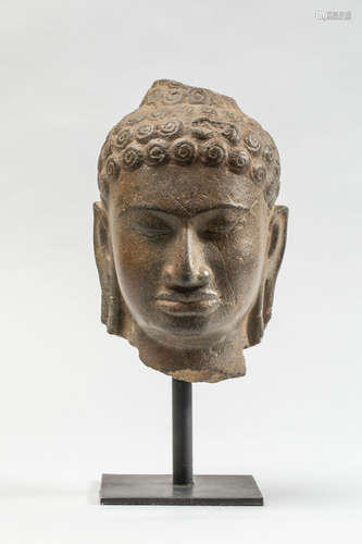 Tête de Buddha à   l’expression sereine coiffée   de large boucles ciselées en une spirale . Pierre grès gris . Thaïlande. Royaume de Dvaravati. 9eme à 11eme siècle .Ht 19cm. Bon état de conversation  malgré une cassure au chignon et aux lobbes d'oreilles