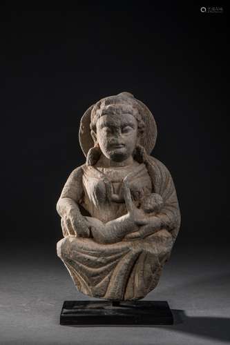 Hariti assise un enfant dans les bras, vêtue d'une robe aux plissés hellénistiques parée d'un pectoral et auréolé d'un nimbe. Elle est la déesse Bouddhique   de l'harmonie, de la famille. Pierre schiste gris. Afghanistan. Art gréco Bouddhique du Gandhara. 2 ème à 3 ème siècle. Ht   24cm. Dépôt calcaire, érosion,   petits états et manques. Provenance ancienne   collection Française 1970