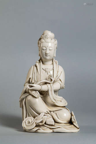 Kwan yin figuré   assis en délassement vêtu   d'une robe monastique à plis bouillonnants, parée d'un pectoral perlé et coiffé d'un chignon tenant dans sa main le sceptre rhui. Porcelaine   blanc de chine de Dehua. Province du Fujuan. Chine. Marque au verso. 24cm.