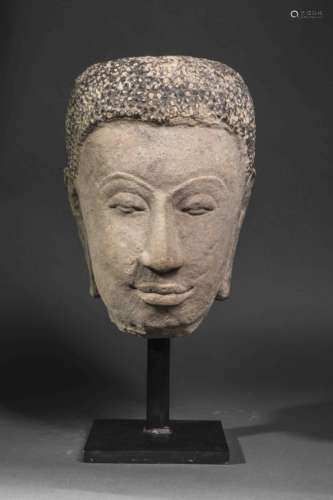 Tête de Buddha exprimant la sérénité, les paupières mi closes préconisant le regard à l'intérieur de soi, la coiffure composée de fines bouclettes.    Pierre grès beige laquée à la coiffe. Thaïlande. Royaume   d'Ayutthaya. 16 ème siècle.   40cm.