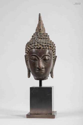 Tête de Buddha a l’expression   sereine , les yeux mi-clos préconisant le regard à l’ intérieur de   soi, la bouche sensuelle exprimant une mou de béatitude,   la coiffure bouclée surmontée   de la protubérance crânienne Ushnisha terminée par un rasmi  flammé. Bronze à patine brune. Thaïlande.   Royaume de Sukhothai .14eme siècle . 20cm. Ancienne   collection Française.