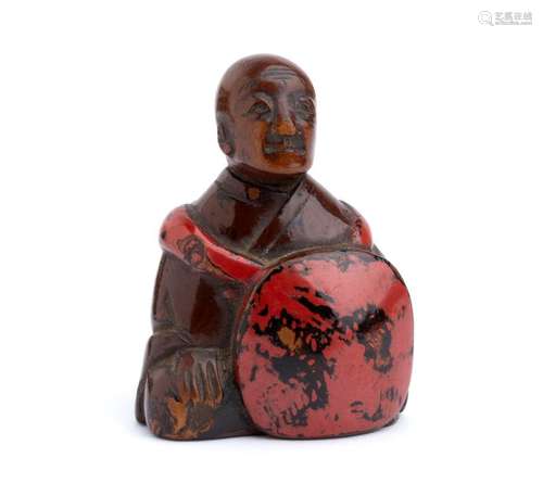 A LACQUERED WOOD NETSUKE OF A SEATED BUDDHIST PRIE...