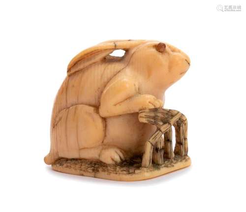 A HORN INLAID IVORY NETSUKE OF A RABBIT AND FENCE ...