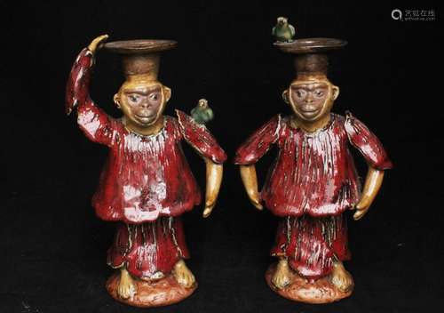 A pair of Chinese Shiwan glaze candlesticks in the form of clothed monkeys with four-character