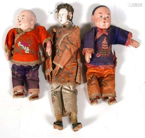 A Chinese painted wooden doll in a silk court robe and two similar children, the largest 25.5cms (