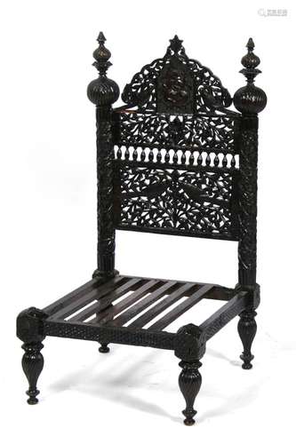 An Indian hardwood low chair profusely pierced and carved with birds, flowers and figures.