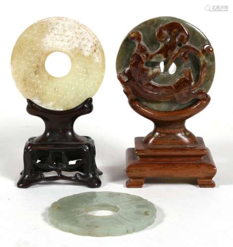 Two Chinese jade bi discs one mounted on hardwood stand together with another carved in relief a