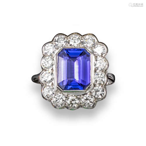 A tanzanite and diamond cluster ring, the emerald-cut tanzanite is rubover-set within a surround