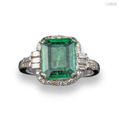An emerald and diamond cluster ring, the emerald-cut emerald is set within a surround of baguette-