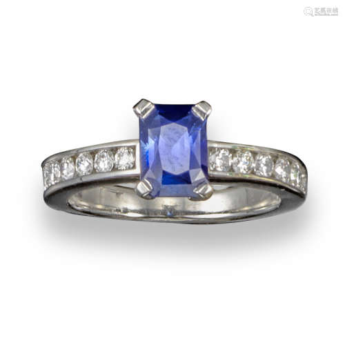 A sapphire and diamond ring, the emerald-cut sapphire is set within channel-set diamond shoulders in