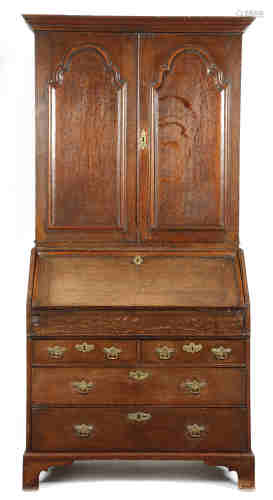 An early 18th century oak bureau cabinet, the moulded cornice above a pair of arched fielded panel