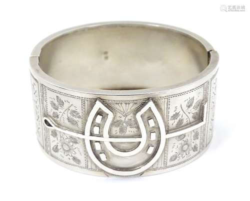 A Victorian silver cuff bracelet of bangle form with horseshoe and floral decoration.