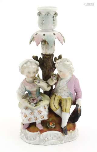 A ceramic candlestick modelled as two children in 18th century dress beneath a tree,