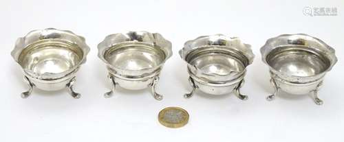 A set of 4 silver salts each with three legs and flared rims.